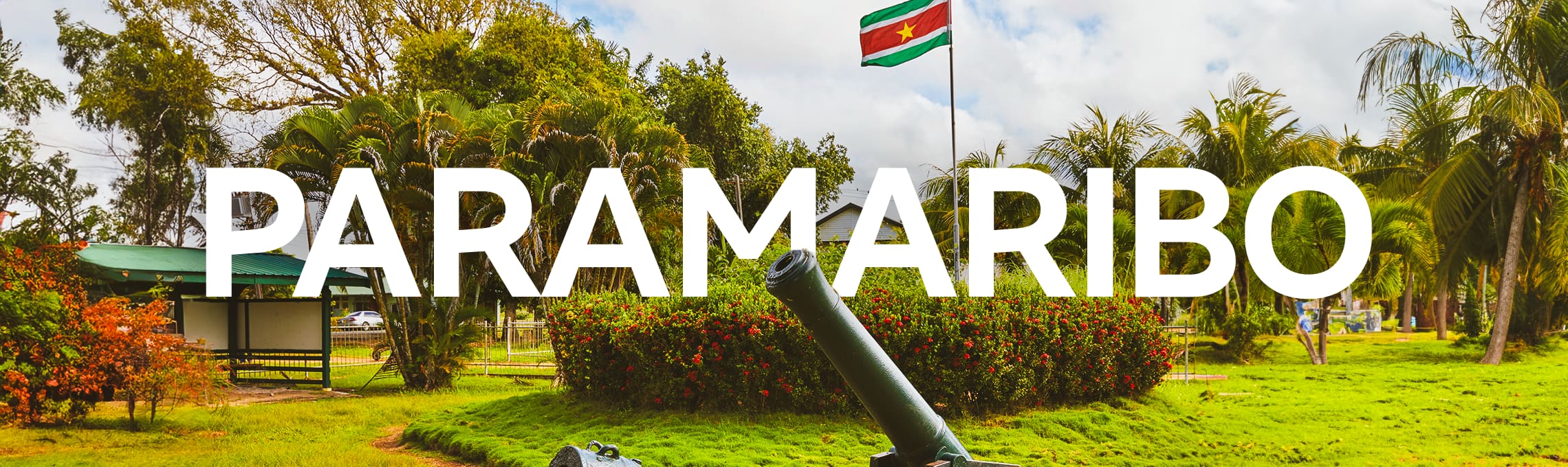 Distrito de Commewijne, com a bandeira da cidade e canhão antigo, e a palavra Paramaribo escrita em letras garrafais brancas.